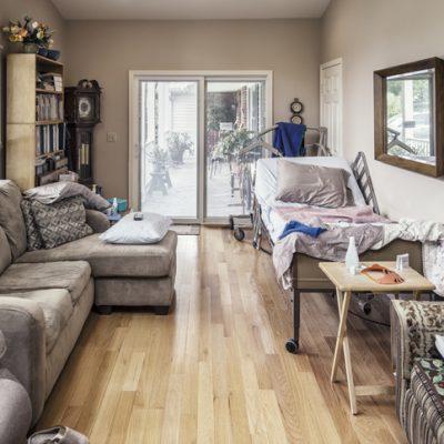 Raised Hospital Bed In Cluttered Private Residence Living Room