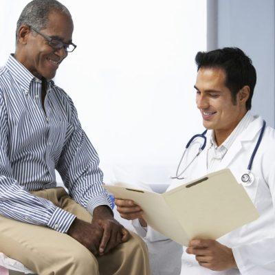 Doctor In Surgery With Male Patient Reading Notes