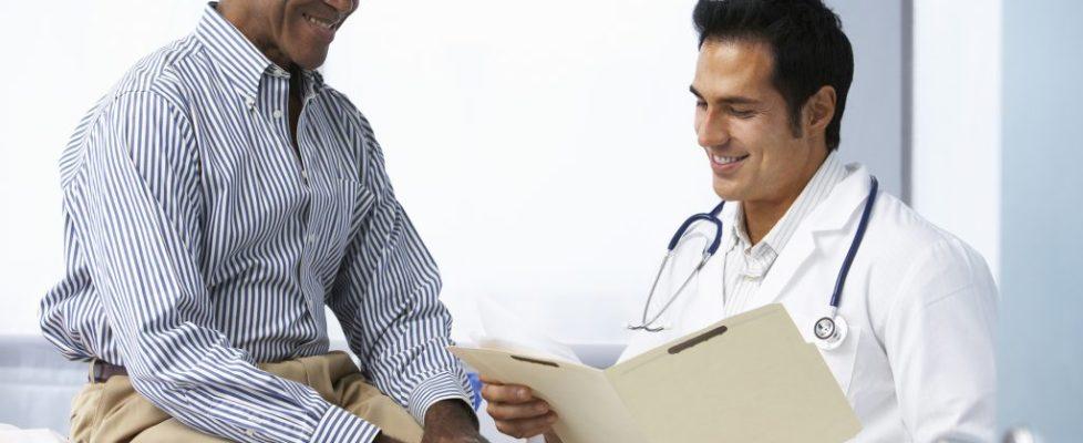 Doctor In Surgery With Male Patient Reading Notes